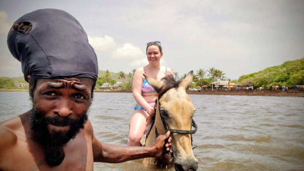 photo of woman horseback riding in the ocean in St. Lucia while local holds the horse
