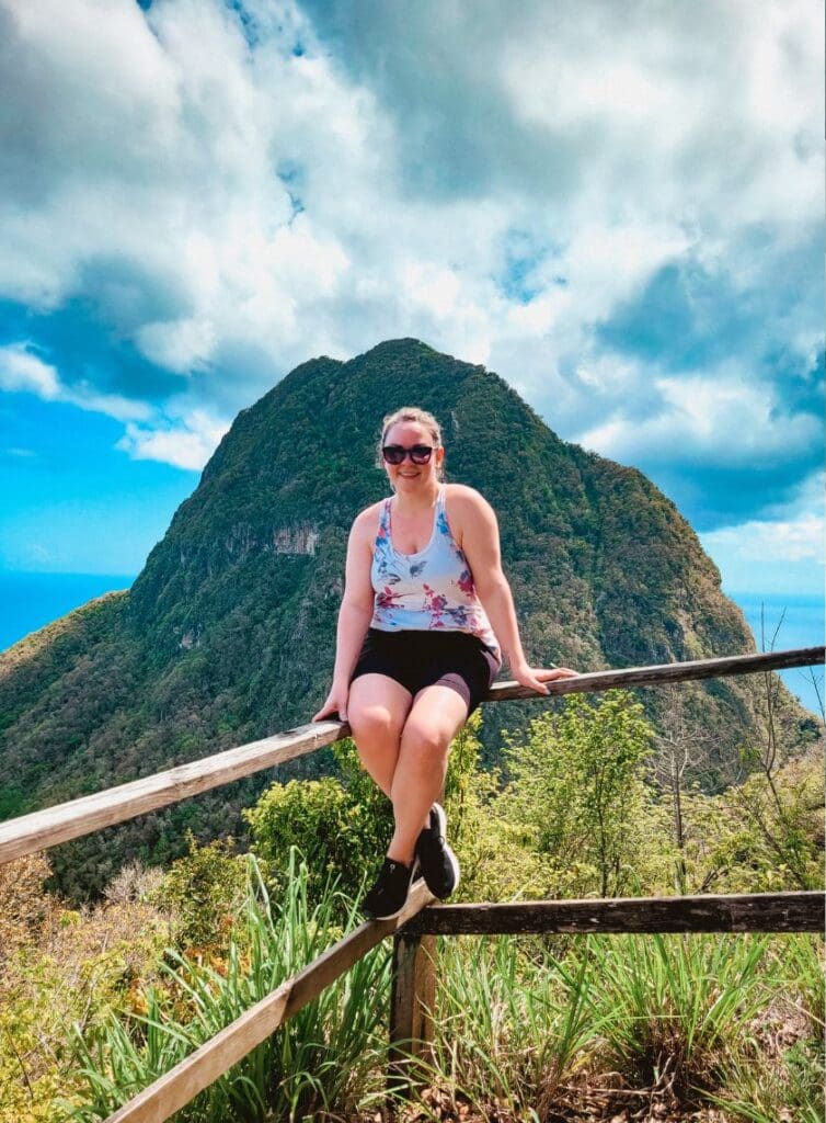 photo of woman sitting along fence line with Petit Piton behind her 