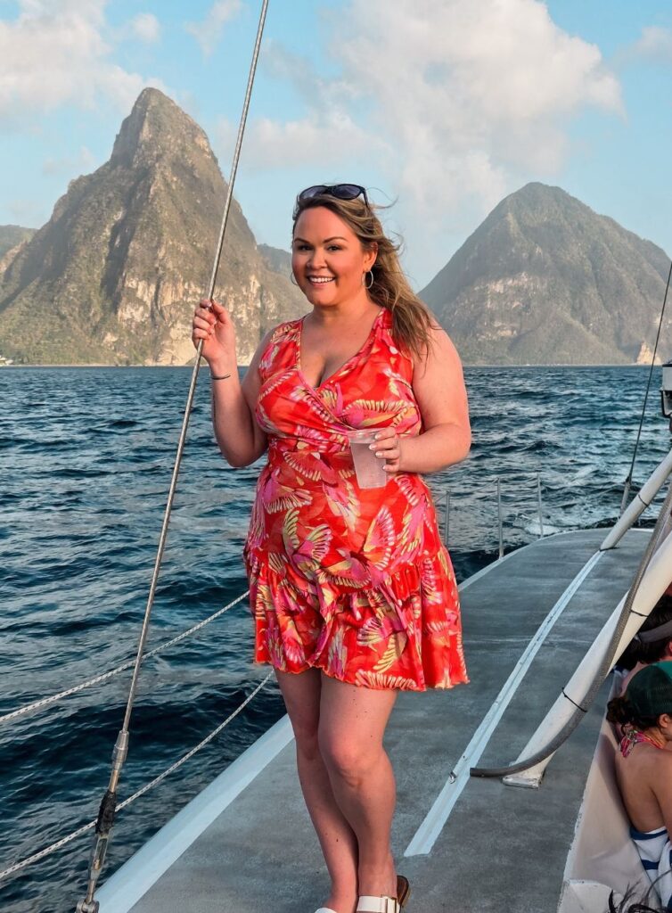 girl posing and holding a cup of water on a catamaran with the Pitons behind her in St. Lucia