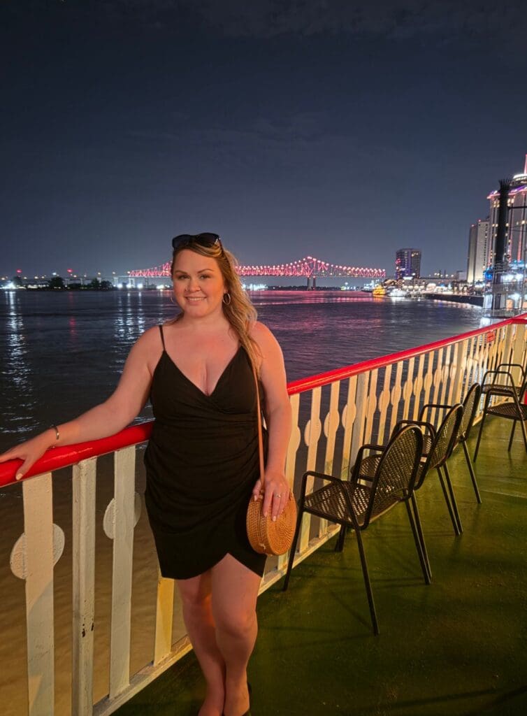 photo of woman smiling on the steamboat with the bridge lit up behind her in NOLA