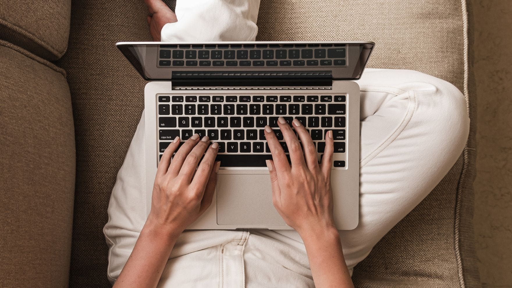 photo of woman on couch typing on laptop